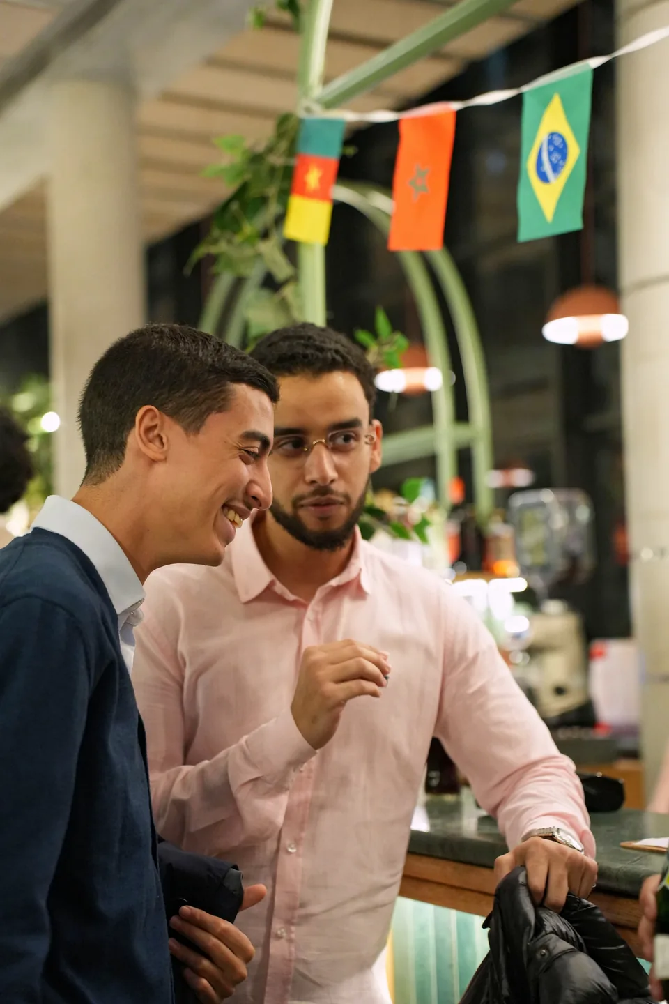 Two young men chat and smile beneath flags of several countries hanging from the ceiling.