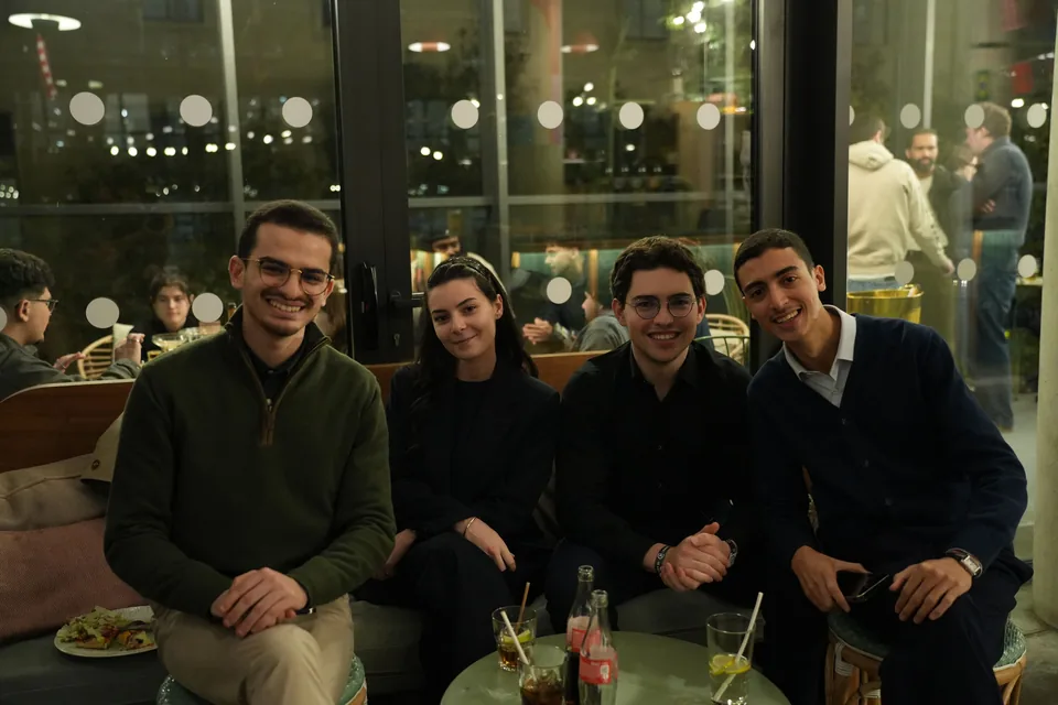 Four young people seated on a banquette smile around a low table set with drinks.