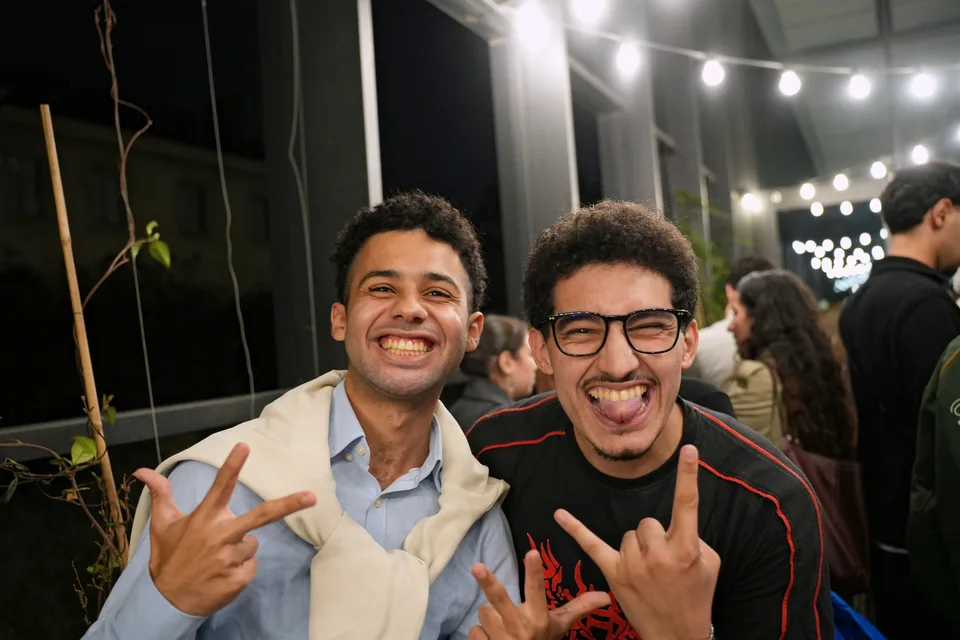 Two young men laugh out loud, making hand signs at the camera.
